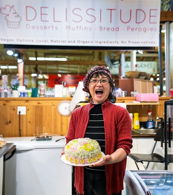 A person holds a cake below the Delissitude sign