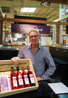 A person smiles holding a wooden case containing 4 bottles of pink wine