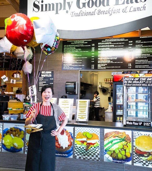 A person in an apron holding balloons in front of Simply Good Eats