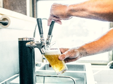 A bartender's arms filling a pint of beer from a tap