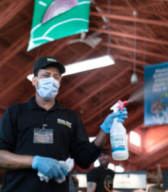 An employee wearing a mask and gloves sprays cleaning solution